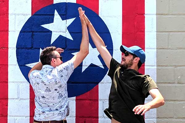 two guys high fiving in front of a nashville flag mural