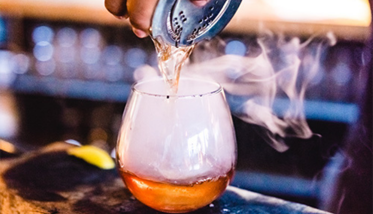 beverage being poured into a glass that has been smoked