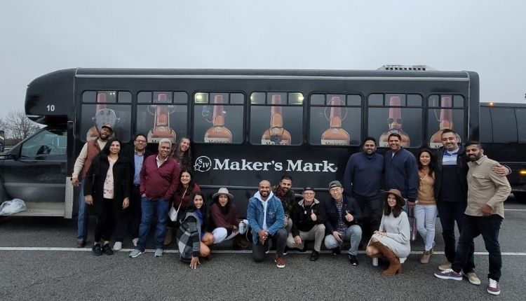 bourbon tasting group in front of a black passenger bus that says "Maker's Mark" on the side