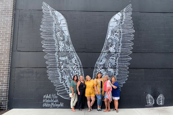 group of women in front of a nashville mural of wings